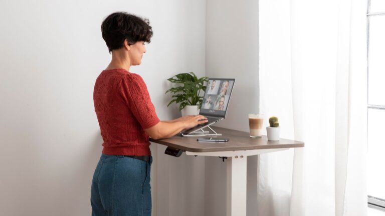 Person arbeitet konzentriert an einem Stehschreibtisch in einem modernen Büro, mit Bildschirm und Arbeitsmaterialien in ruhiger, professioneller Arbeitsatmosphäre.