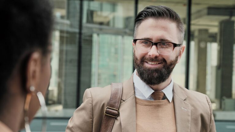 Ein Buisness Mann mit Brille lächelt eine Kollegin auf de Straße an