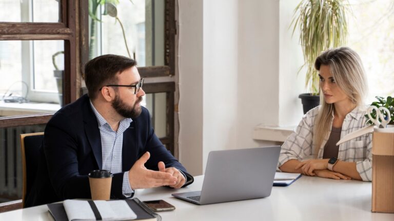 Zwei Personen sitzen sich an einem Tisch in einem modernen Büro gegenüber und führen ein ruhiges Gespräch