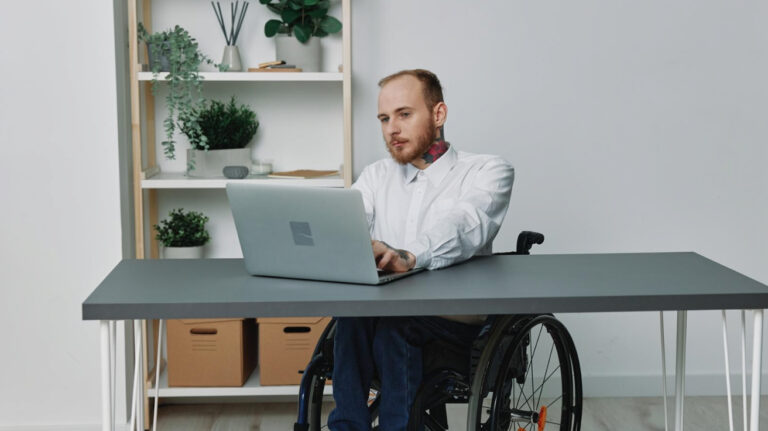 Betriebliches Eingliederungsmanagement BEM: Ein junger Mann im Rollstuhl vor seinem PC-Arbeitsplatz.