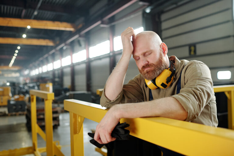 Tired or sick bald engineer touching his head while leaning by bar at break