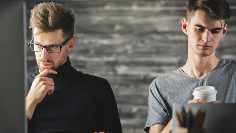 zwei Männer sitzen am Schreibtisch und arbeiten am Laptop