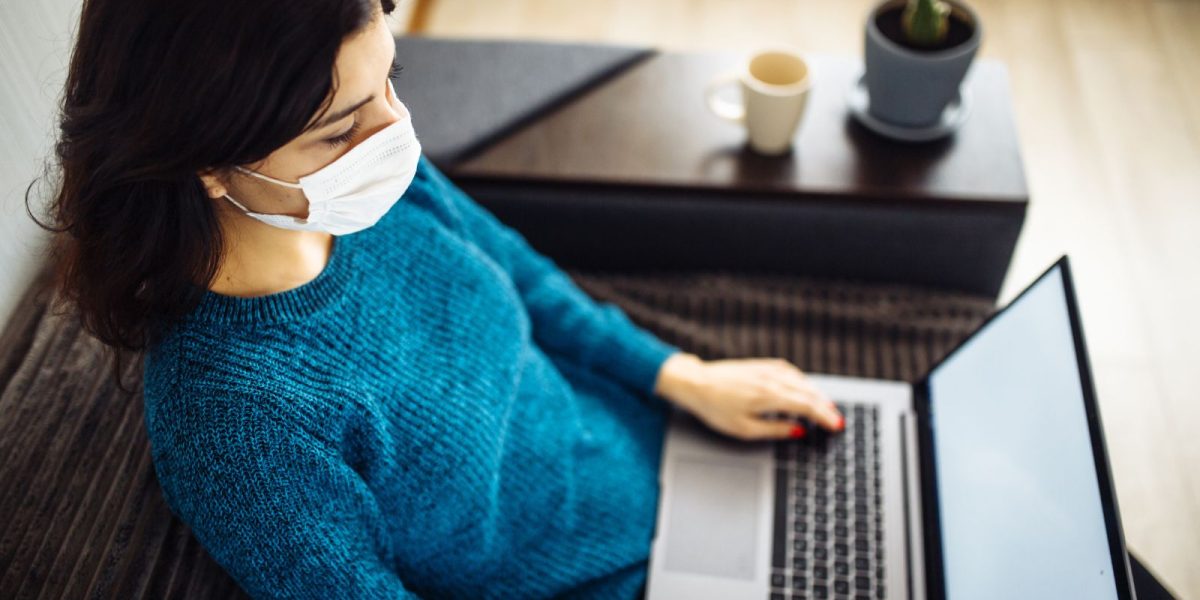 Frau mit Maske schaut auf einen Laptop