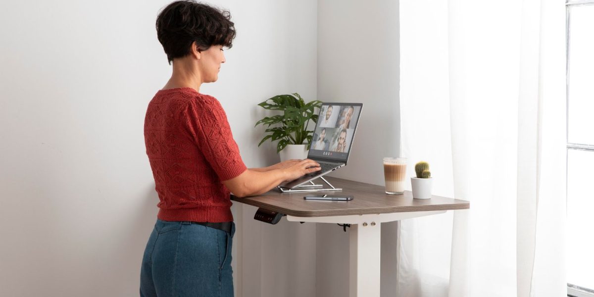 Person arbeitet konzentriert an einem Stehschreibtisch in einem modernen Büro, mit Bildschirm und Arbeitsmaterialien in ruhiger, professioneller Arbeitsatmosphäre.