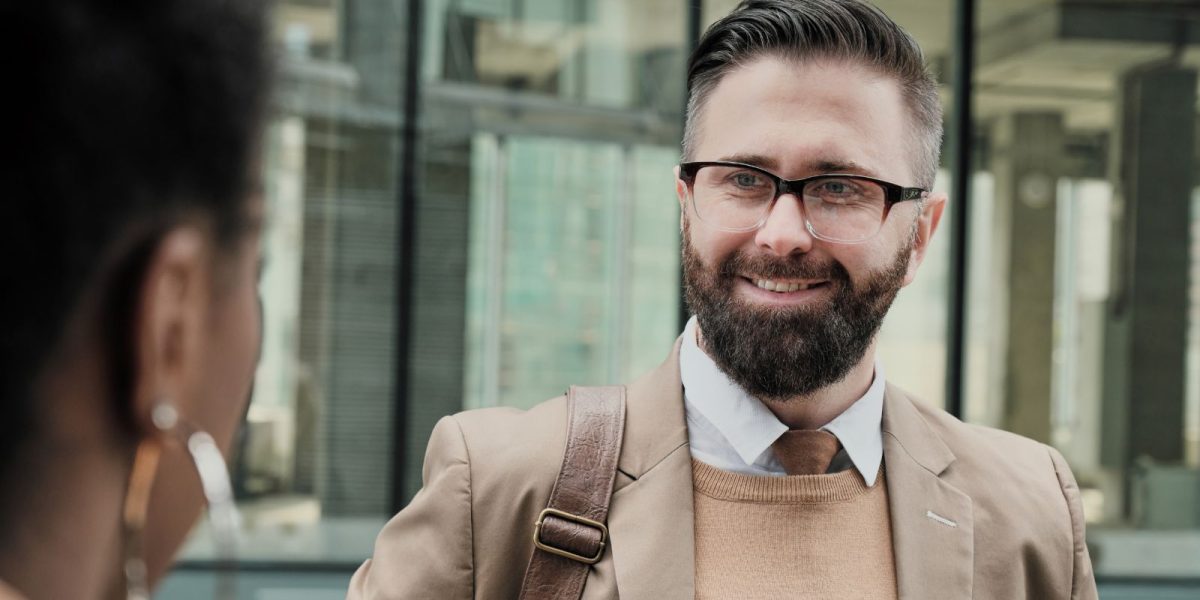 Ein Buisness Mann mit Brille lächelt eine Kollegin auf de Straße an
