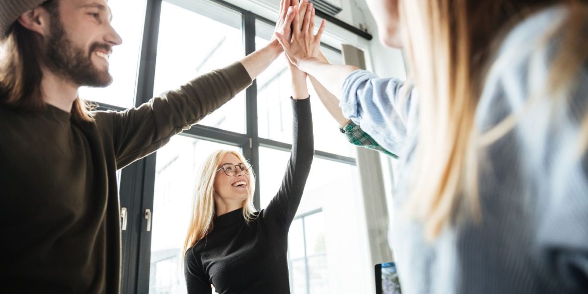 Büro mit Fenstern gibt sich eine lächelnde Gruppe highfive