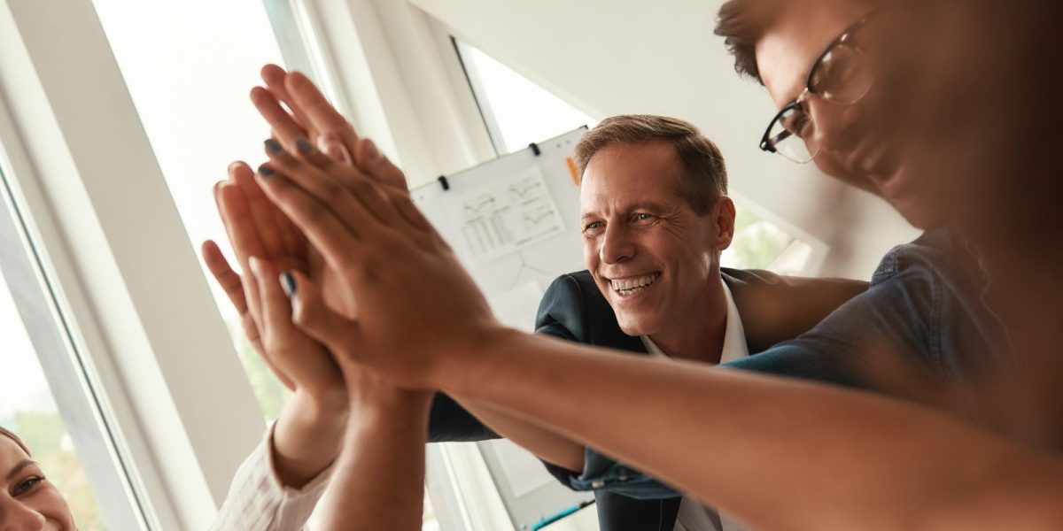 Lächelnde Kollegen geben sich im Büro high five mit fensterlicht