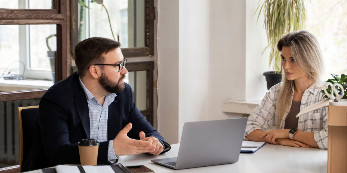 Zwei Personen sitzen sich an einem Tisch in einem modernen Büro gegenüber und führen ein ruhiges Gespräch