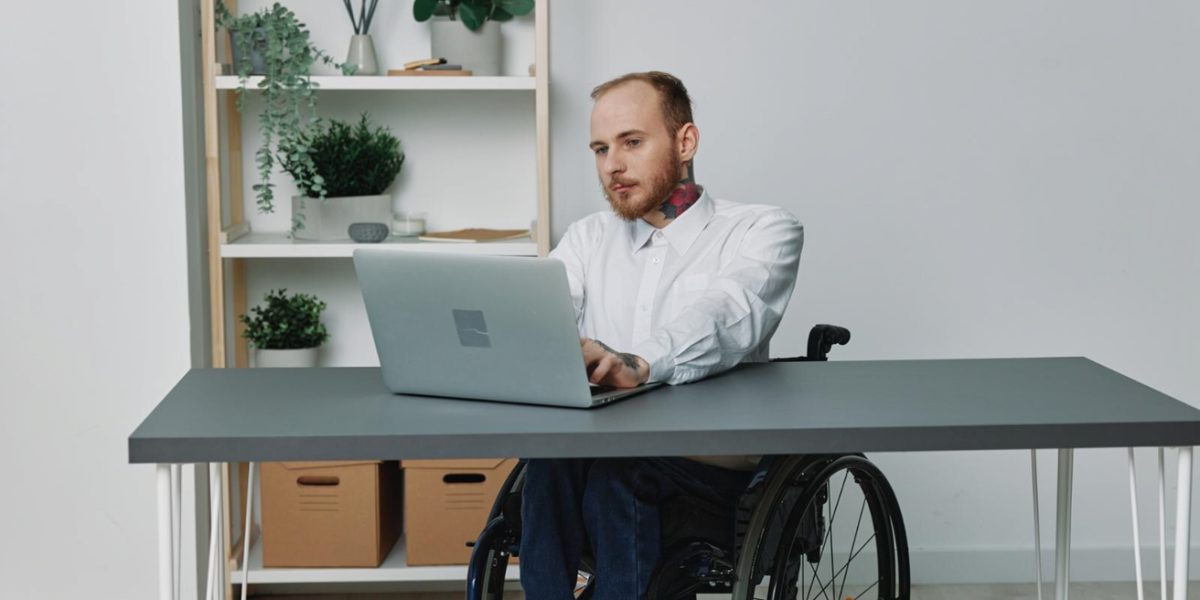 Betriebliches Eingliederungsmanagement BEM: Ein junger Mann im Rollstuhl vor seinem PC-Arbeitsplatz.