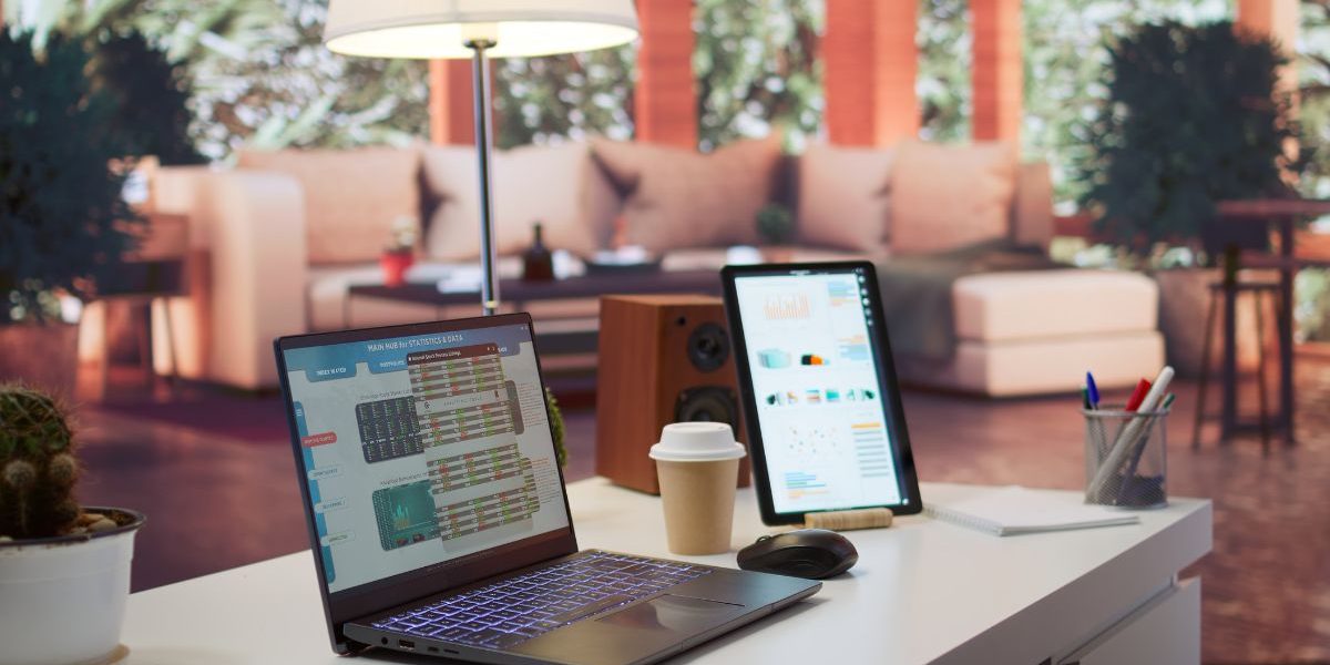 Moderner Büroarbeitsplatz mit Laptop und Tablet auf einem hellen Schreibtisch, daneben Kaffeebecher, Maus und Stifte; im Hintergrund ein ruhiger, wohnlich gestalteter Raum mit warmem Licht und Pflanzen.